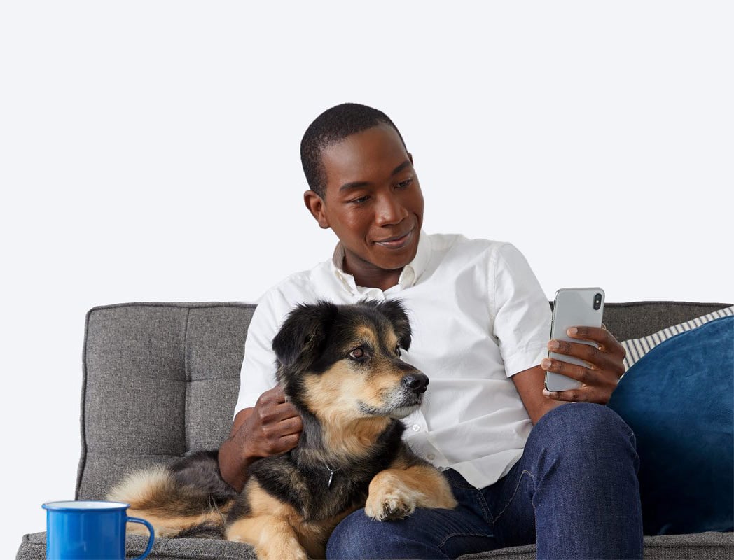 A man and dog on couch, looking at the man's phone.