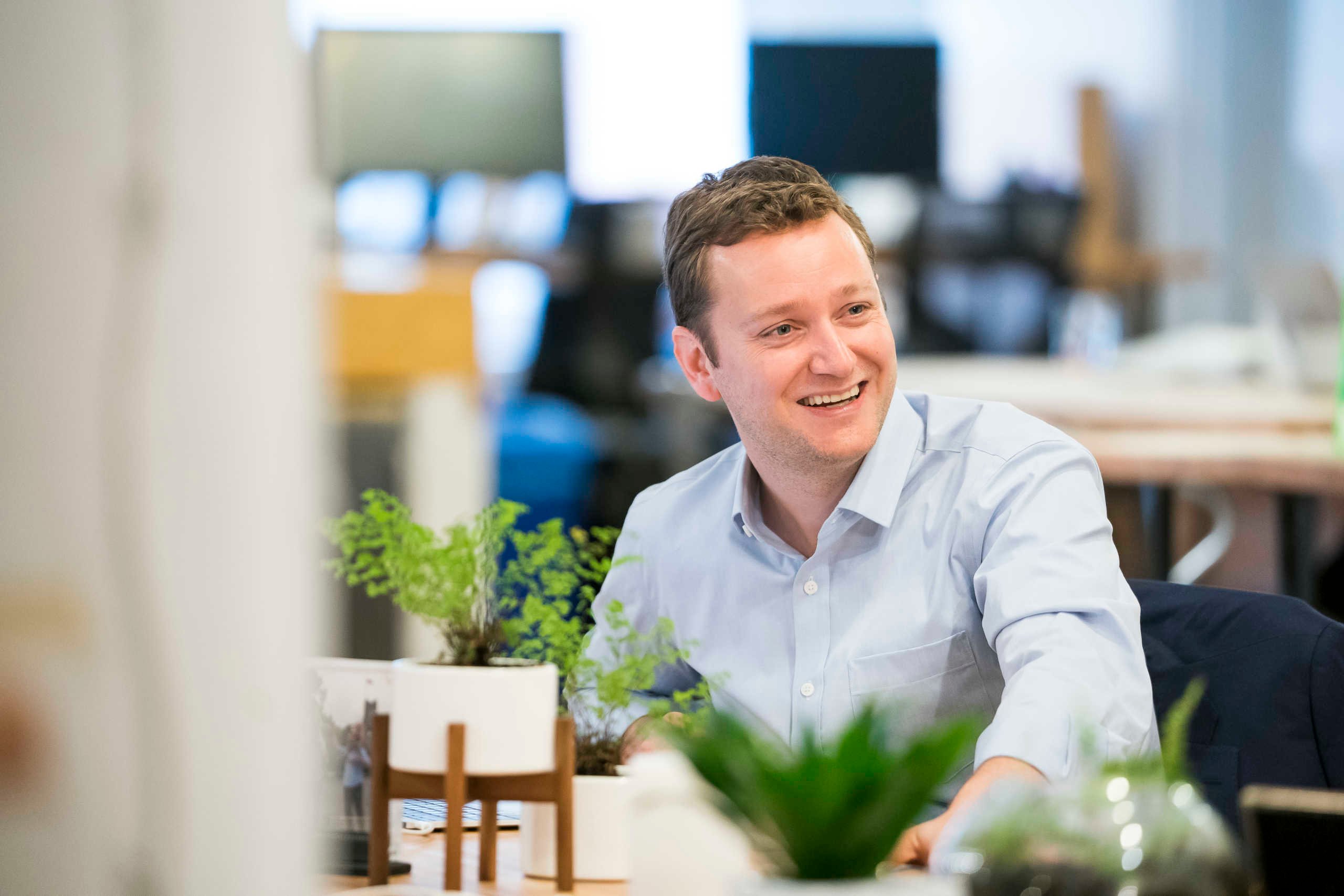 Man sitting at a desk in an office, smiling while looking off to the right..