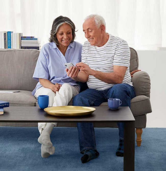 A man and woman sitting on a couch looking at the man's phone together.